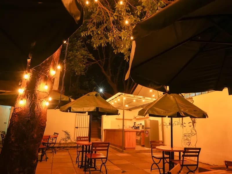 The coffee shop terrace at night, with umbrellas, wooden tables and string lights in a tree
